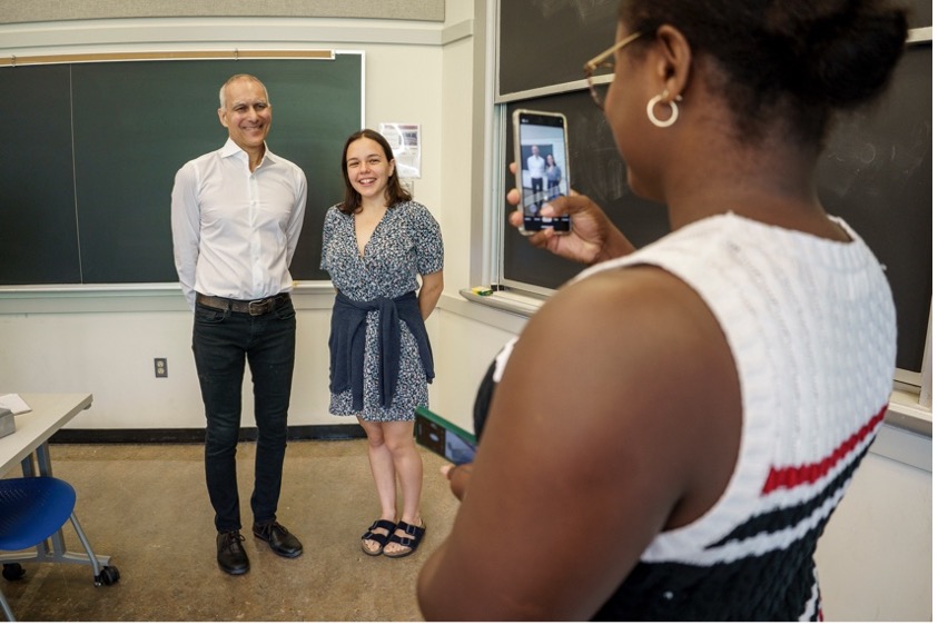 Moungi Bawendi poses with an MIT student. Another student in the foreground, with her back to the camera, holds out her phone to take the photo.