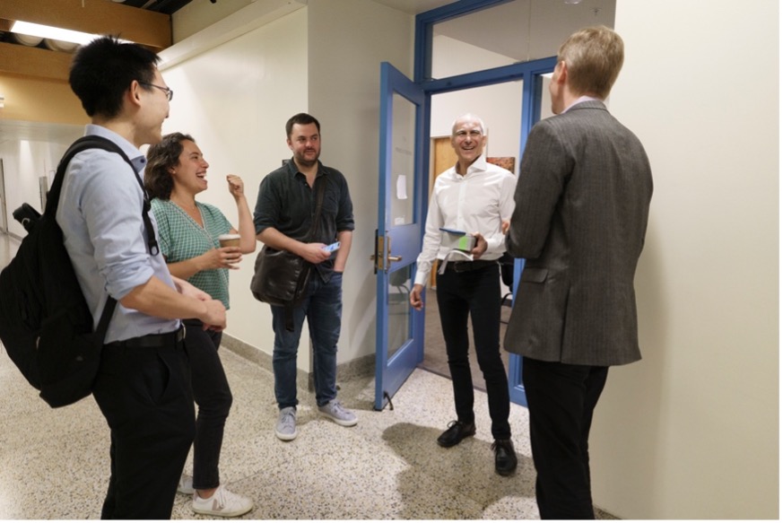 Moungi Bawendi talks and laughs with three other students and faculty member outside a classroom.