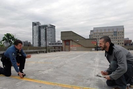 Sgt. Cheryl Vossmer of the MIT Police, left, and Libraries Administrative Assistant and Public Service Support Associate Ryan Gray measure parking space atop West Garage where vegetables, flowers and herbs will take the place of cars in MIT's first-ever community garden.