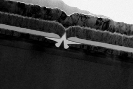 A cross-section transmission electron micrograph of the fabricated transistor. The central inverted V is the gate. The two molybdenum contacts on either side are the source and drain of the transistor. The channel is the indium gallium arsenide light color layer under the source, drain and gate.