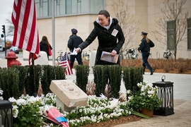 A visitor places a paper crane on a temporary memorial erected in honor of MIT Police Officer Sean Collier, near the spot where his life was taken. The temporary marker will be replaced by a permanent memorial, whose design was unveiled on Friday, to be built over the coming months.