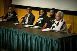 Five people sit at stage behind table with microphones