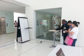 Students in the MIT Media Lab try out a pen-controlled "writing" drone. When users trace lines on a desk with an inkless pen, the drone will duplicate those lines on a distant whiteboard. This is done with cameras tracking the pen and drone, and software synching the two patterns.  