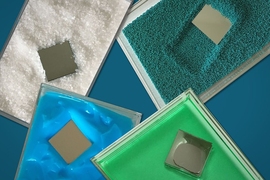 The photograph shows a square-shaped “intruder” plunging through various material, including coarse, salt-like grains (white) and fine sand (blueish green), as well as more viscous (green) and pasty (blue) materials. 
