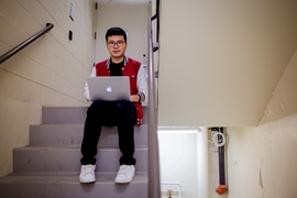 CEE postdoc Hao Sun sits in a stairwell in the Green Building. On the right attached to the ceiling is one of the accelerometers used to monitor the building.  
