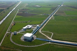 An aerial view of the Virgo site shows the Mode-Cleaner building, the Central building, the 3km-long west arm and the beginning of the north arm. The other buildings include offices, workshops, computer rooms and the control room of the interferometer.