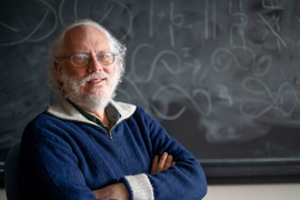 Peter Shore smiles with arms crossed to camera in front of a chalkboard