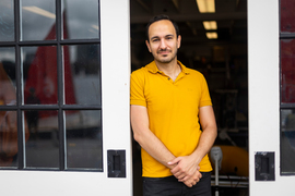 Fadel Adib stands between 2 glass panel sliding doors while wearing a yellow shirt and black pants.