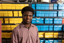 Ajisafe smiles with yellow and blue containers on shelves in background.