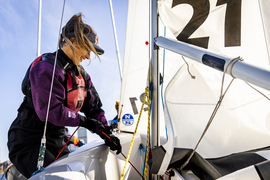 A community member in sailing gear gets their boat ready by pulling a rope tightly.