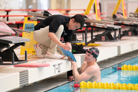 At the Z Center pool, Lu, left, shows an iPad to Borisov. Lu is on the edge of the pool and leaning over, and Borisov is inside the pool wearing a swim cap while staring at the iPad.