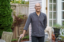 Moungi Bawendi stands outside his home, with his dog in the background.