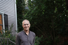 Moungi Bawendi, casually dressed and barefoot, stands outside his home.