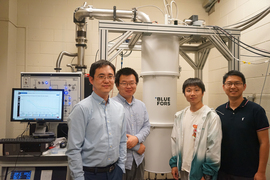 Four team members stand inside the lab around large white pipe and laptop.