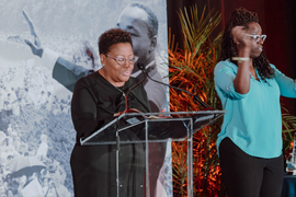 DiOnetta Jones Crayton stands on stage with an interpreter. A greyscale photo of Martin Luther King Jr. at the 1963 March on Washington is in the background.