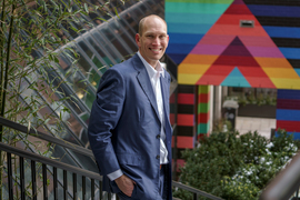 Robin Scheffler portrait as he stands outside on stairs, with colorful mural in background, near Kendall-MIT station.