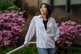 Cindy Xie smiles outside and looks up and to the side. The background has blooming pink rhododendrons.