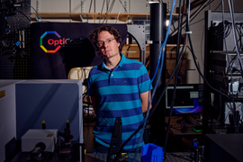 Riccardo Comin stands in his lab, filled with cables and large equipment.