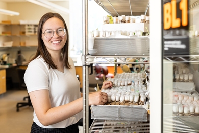 Portrait photo of Payton Dupuis standing near a rack of fruit fly vials in a lab