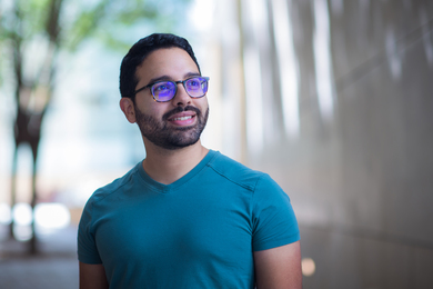 Photo of Raúl Mojica Soto-Albors standing outside with blurry background. He looks to the upper right. His glasses have subtle purple reflections.