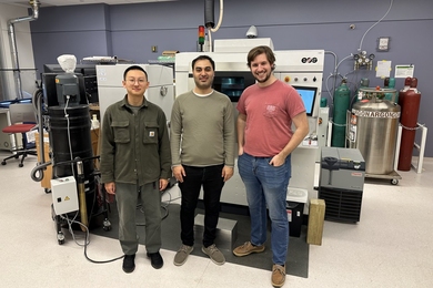 Three researchers stand side by side in front of a piece of heavy equipment in a lab.